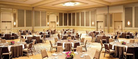 Un amplio salón de banquetes con mesas redondas y sillas, dispuesto en una distribución simétrica.