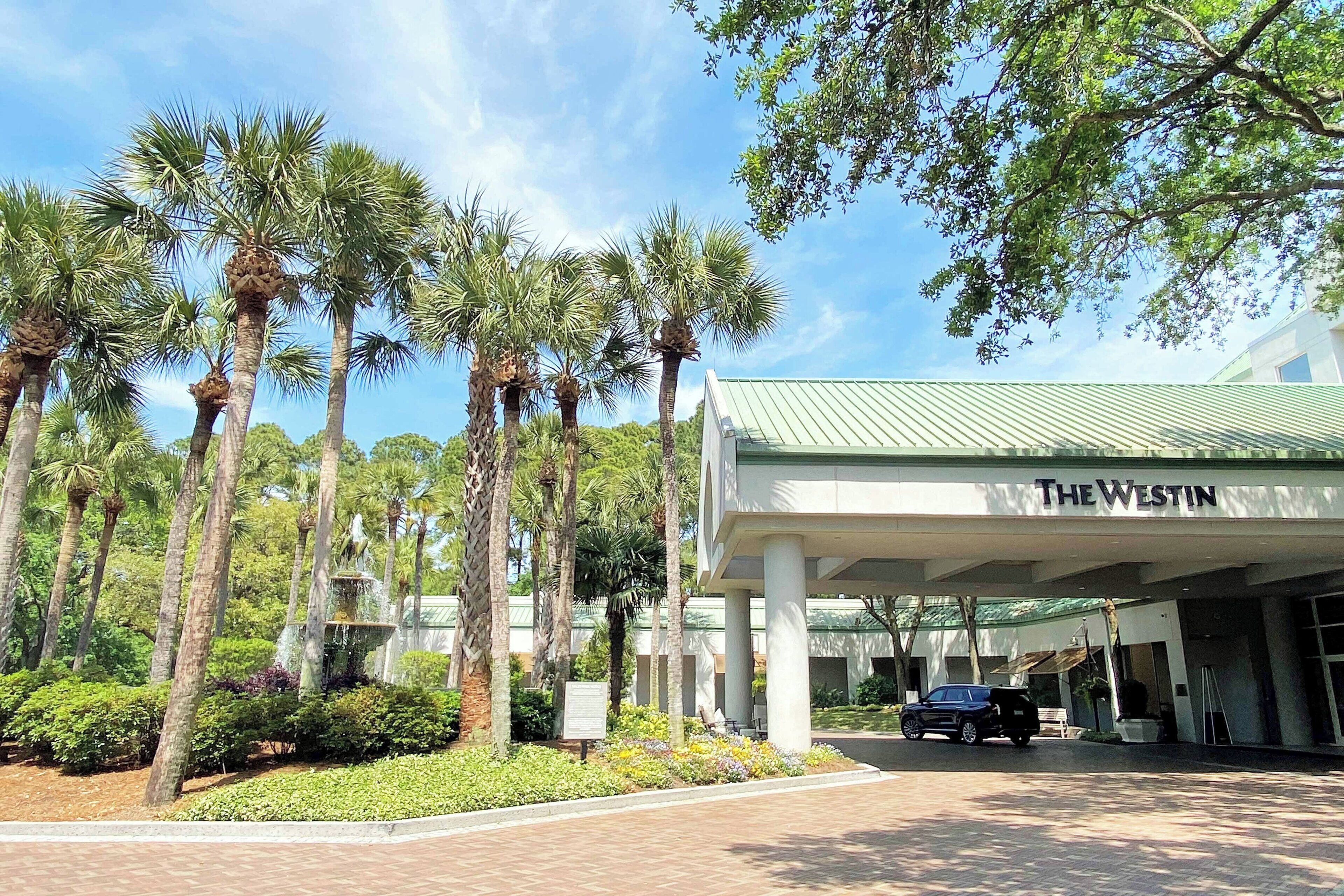 A hotel entrance with palm trees and a car parked in front.