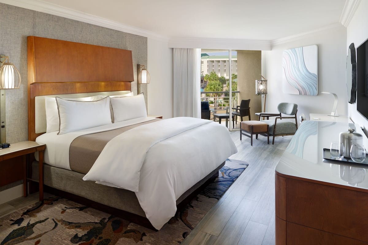 Ein Hotelzimmer mit einem großen Bett, einem Schreibtisch, einem Stuhl, einem Fernseher und Blick nach draußen.