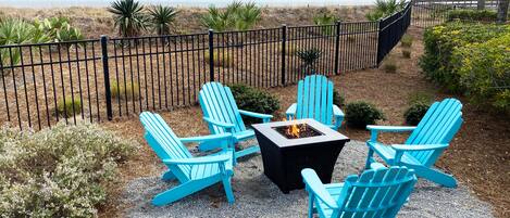 Une terrasse avec quatre chaises Adirondack bleues et une table carrée autour d’un foyer extérieur.