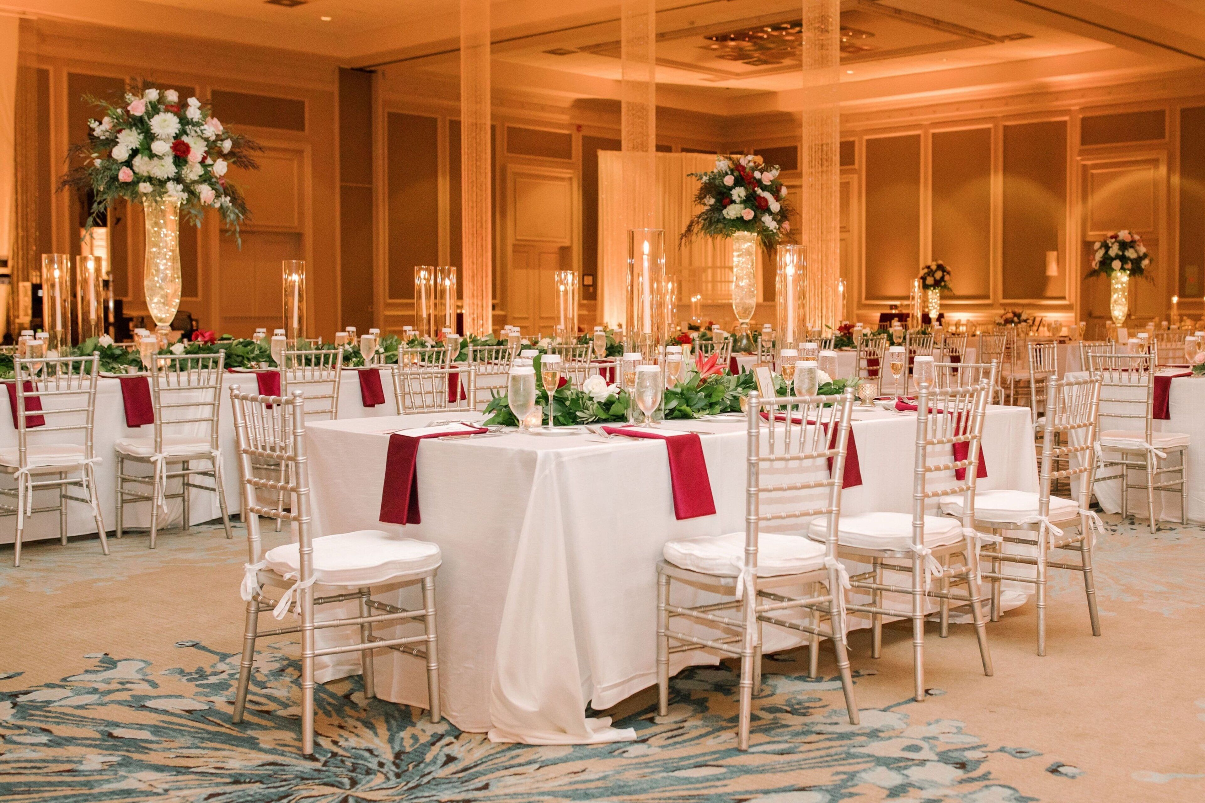 A banquet hall with round tables, white chairs, and red tablecloths.