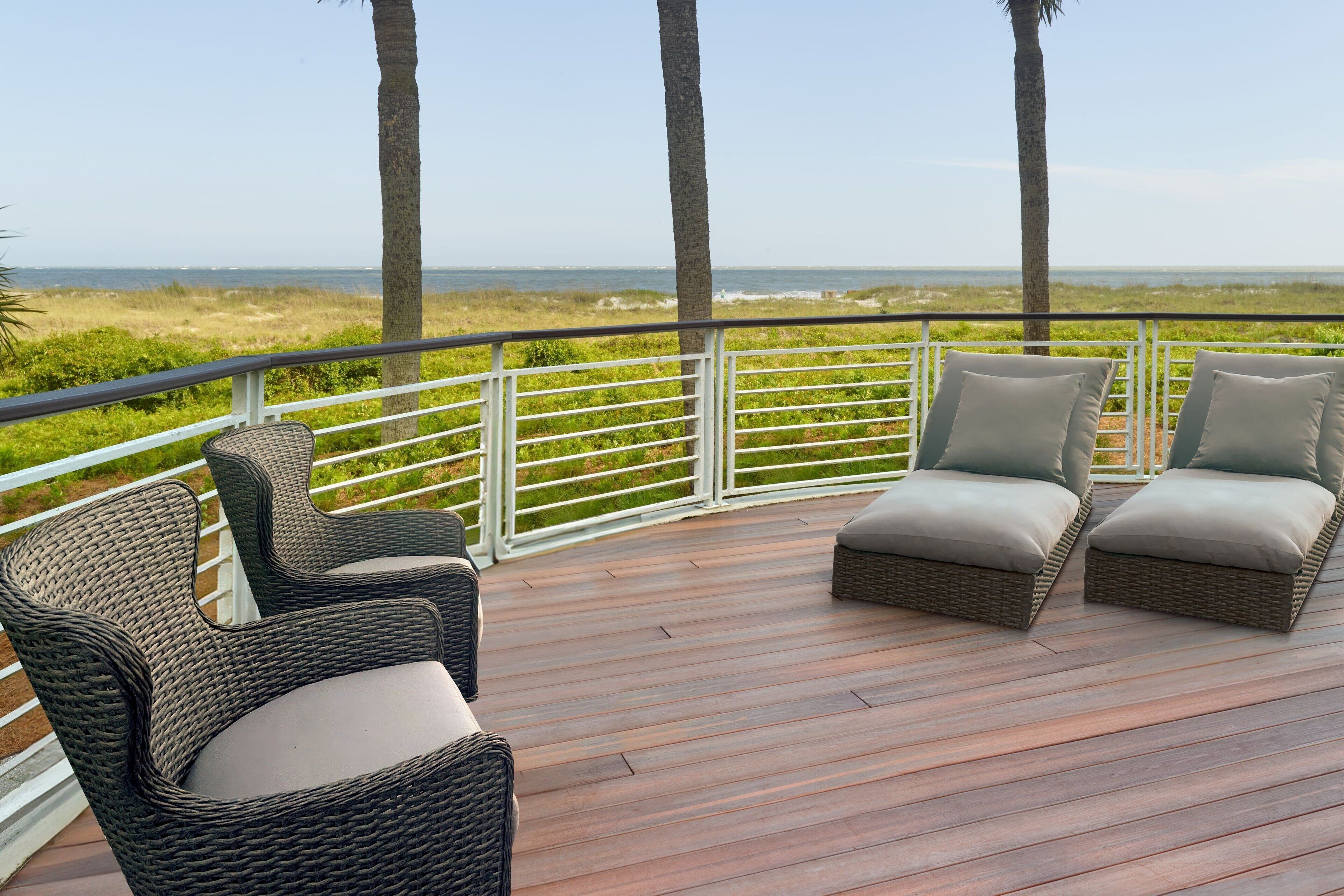 A deck with wicker furniture and a view of the beach.