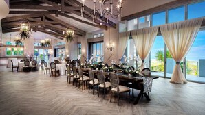 Une salle à manger spacieuse avec un plancher en bois, une longue table dressée pour le repas et de grandes fenêtres offrant une vue sur l’extérieur.