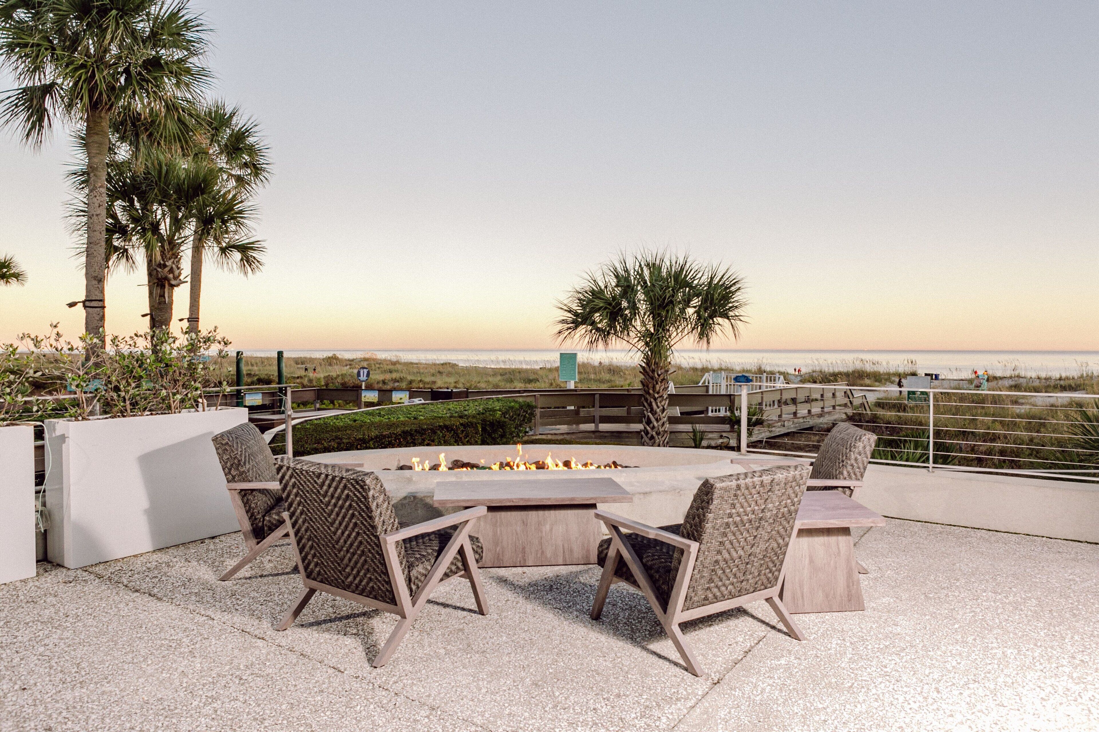 An outdoor patio with a fire pit, seating, and a view of the beach.