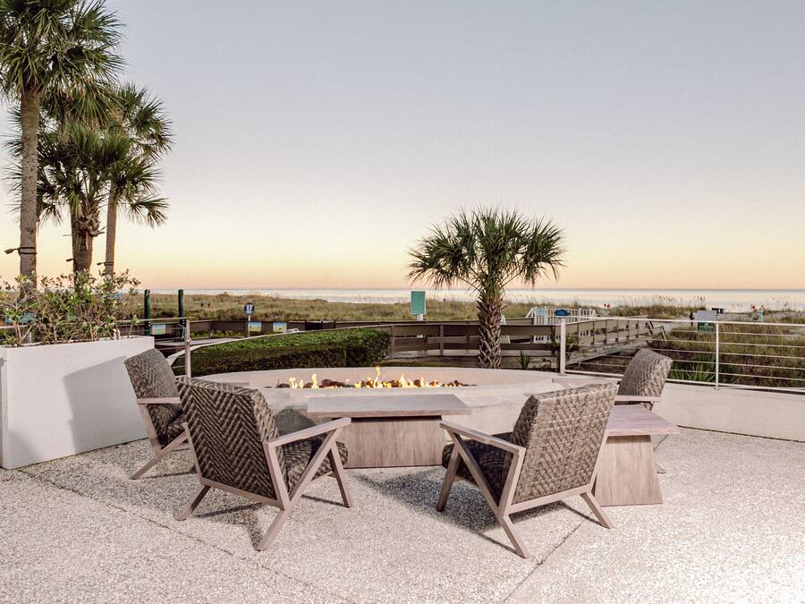 An outdoor patio with a fire pit, seating, and a view of the beach.