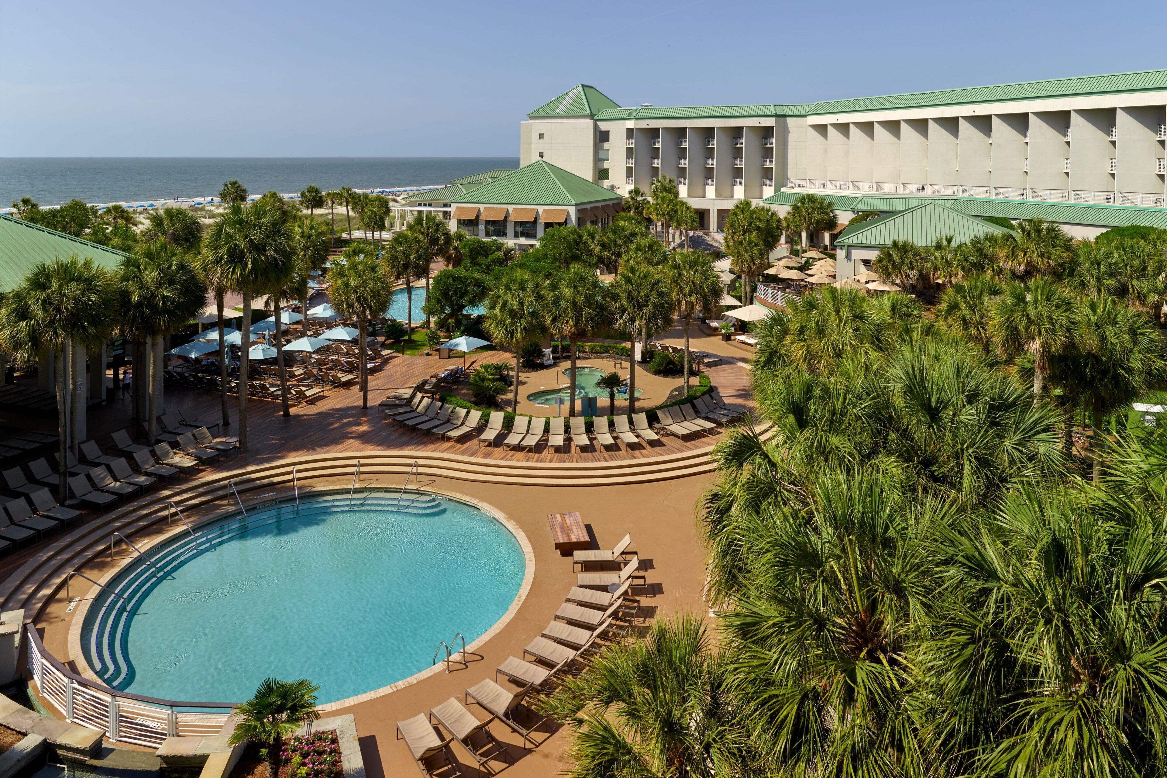 Un resort con una gran piscina, áreas de descanso y vista al océano.
