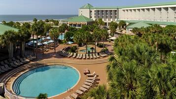 A resort with a large pool, lounge areas, and a view of the ocean.
