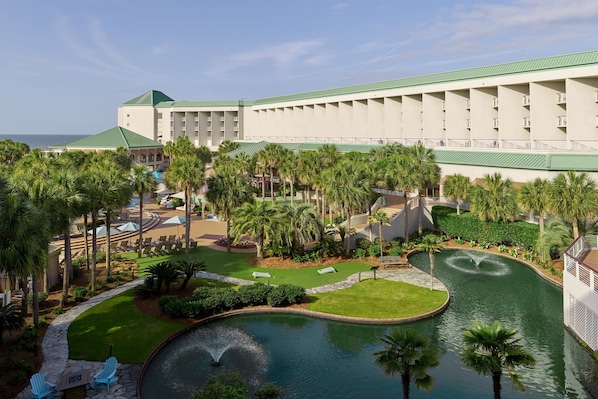 A hotel with a large building, palm trees, a swimming pool, and a fountain.