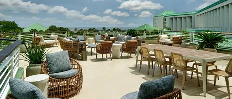 A rooftop terrace with wicker furniture, a dining table, and a view of the ocean.