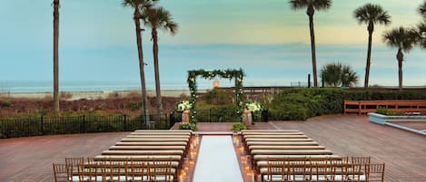 An outdoor wedding setup with a wooden deck, white aisle, and chairs arranged for guests.