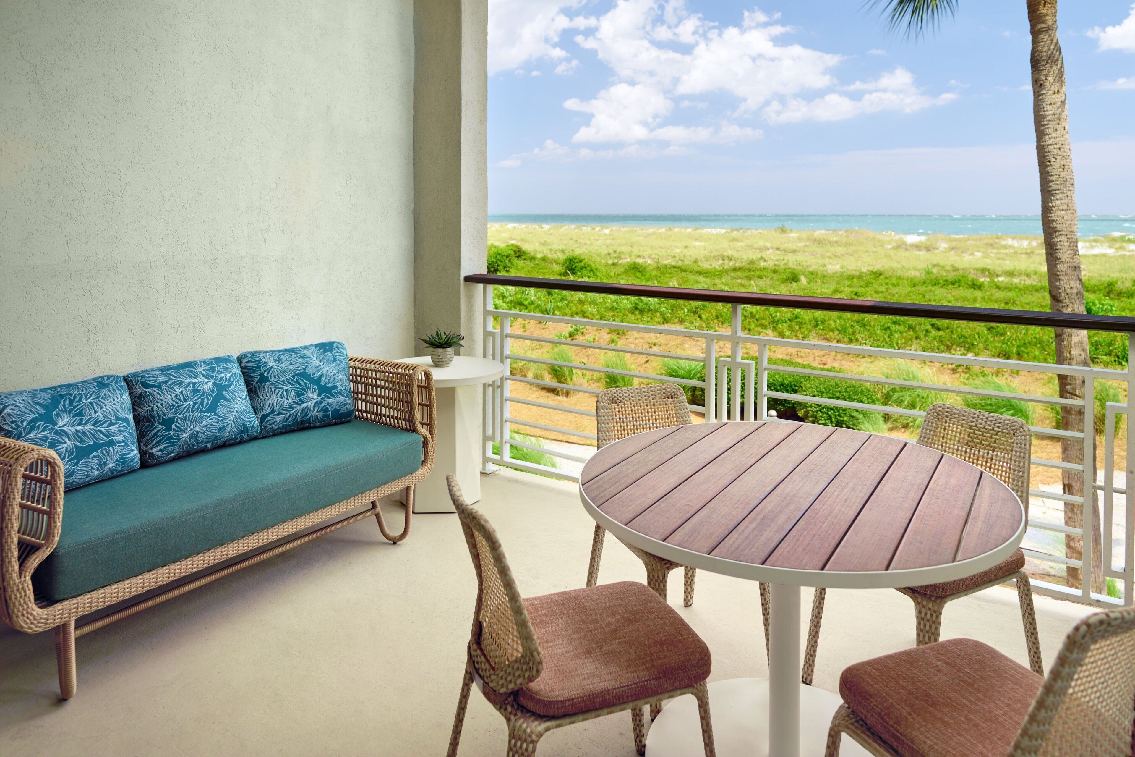 A balcony with a wicker sofa, a round wooden table, and wicker chairs.