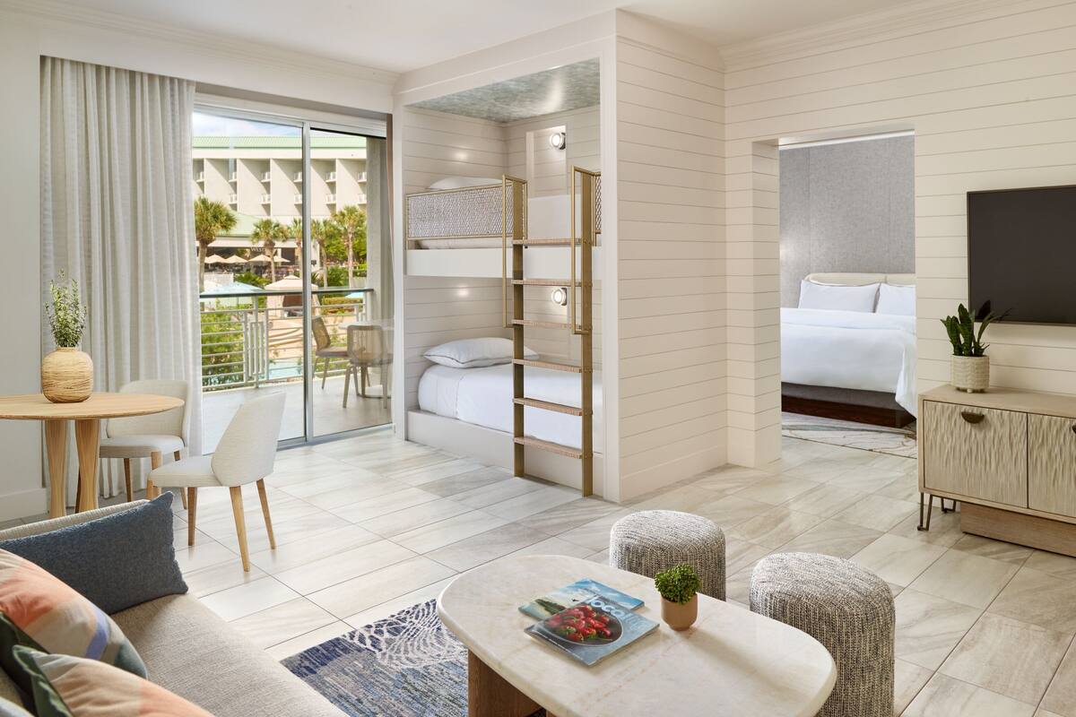 Ein modernes Hotelzimmer mit Balkon, einer Couch, einem Esstisch und einem Bett.