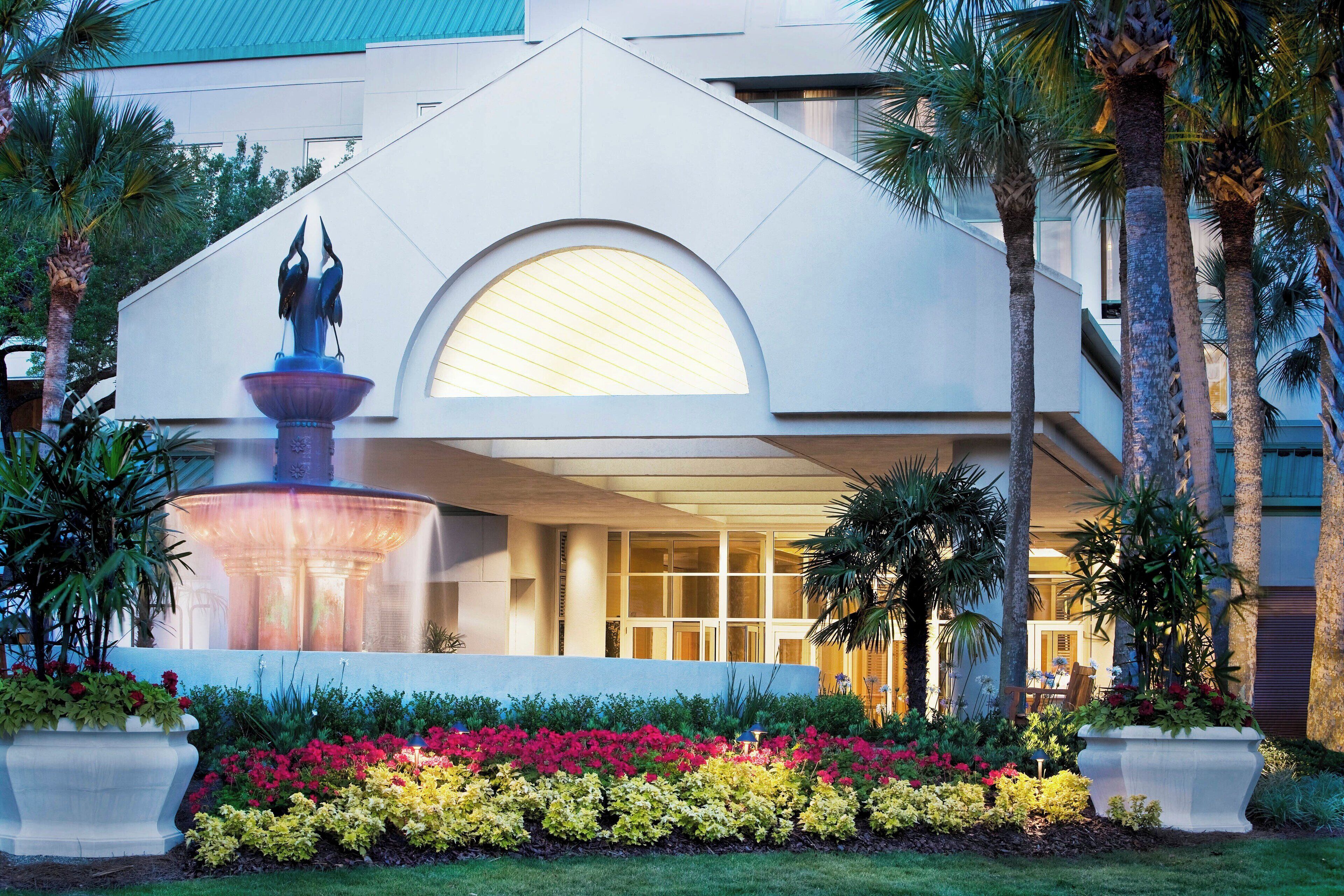 A modern hotel with a fountain, palm trees, and a well-maintained garden.
