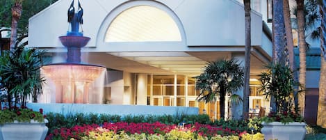A modern hotel with a fountain, palm trees, and a well-maintained garden.