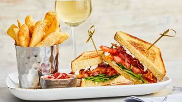A sandwich cut in half with visible ingredients, a glass of white wine, and a container of fries.