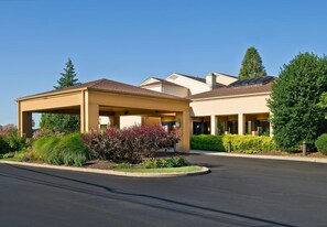 Welcome to our hotel, featuring a covered entrance and main building with a flat roof, set amidst beautifully landscaped grounds.
