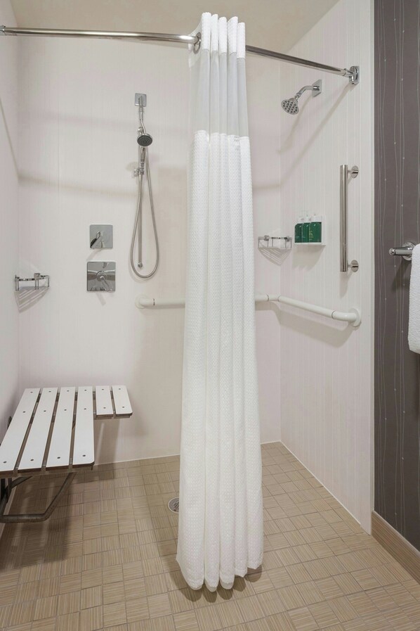 Un baño moderno con ducha, barras de apoyo, un asiento y un perchero para toallas.