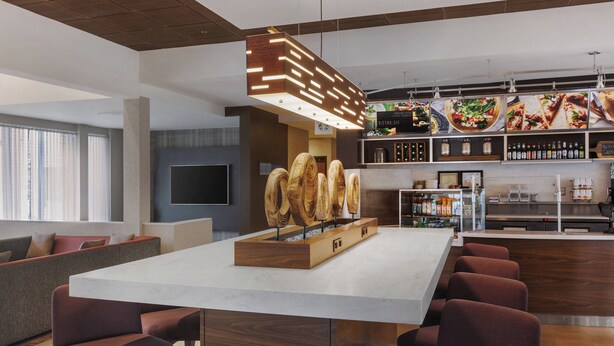 A modern bar area with a central island, seating, and a variety of food and drink displays. - Courtyard by Marriott Philadelphia Willow Grove (Willow Grove)