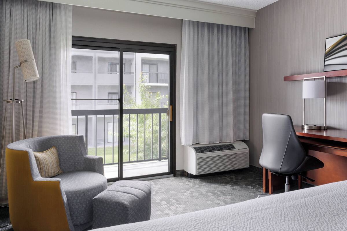 A hotel room with a large sliding glass door to the balcony, a desk, a chair, and a bed.