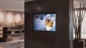 A modern interior with a digital screen advertising a new bistro bar, a wooden shelf with decorative items, and a tall vase with branches. - Courtyard by Marriott Philadelphia Willow Grove (Willow Grove)