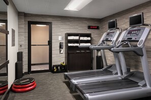 Un gimnasio con cintas de correr, un reloj digital y una zona de almacenamiento con toallas.