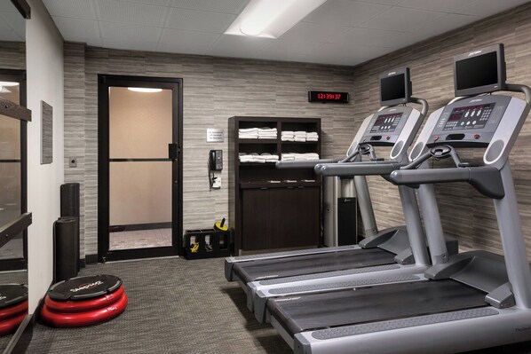 A gym with treadmills, a digital clock, and a storage area with towels.