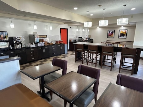 A modern kitchen with dark cabinets, a red door, and a dining area with wooden tables and chairs.. Best Western Forsyth - Decatur