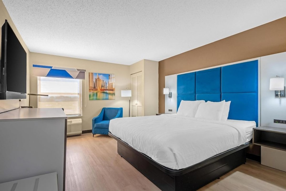 Een hotelkamer met een bed, een bureau, een stoel, een televisie en een schilderij aan de muur.