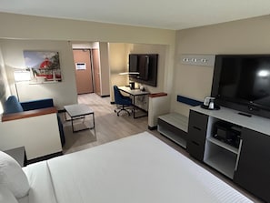 Ein Hotelzimmer mit Bett, Schreibtisch mit Stuhl, Fernseher und einer kleinen Sitzecke.