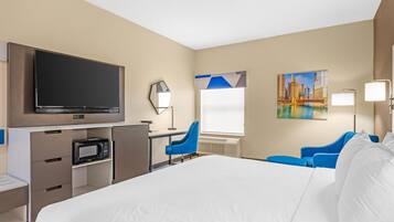 Une chambre d’hôtel avec un lit, un bureau doté d’un téléviseur à écran plat, un four à micro-ondes, une chaise bleue et un tableau accroché au mur.