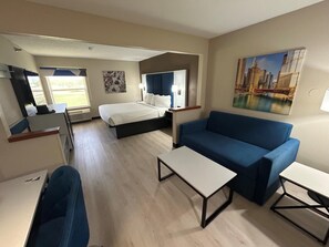 A hotel room with a bed, a blue sofa, a small table, a TV, and a painting on the wall. - Best Western Forsyth - Decatur (Forsyth)