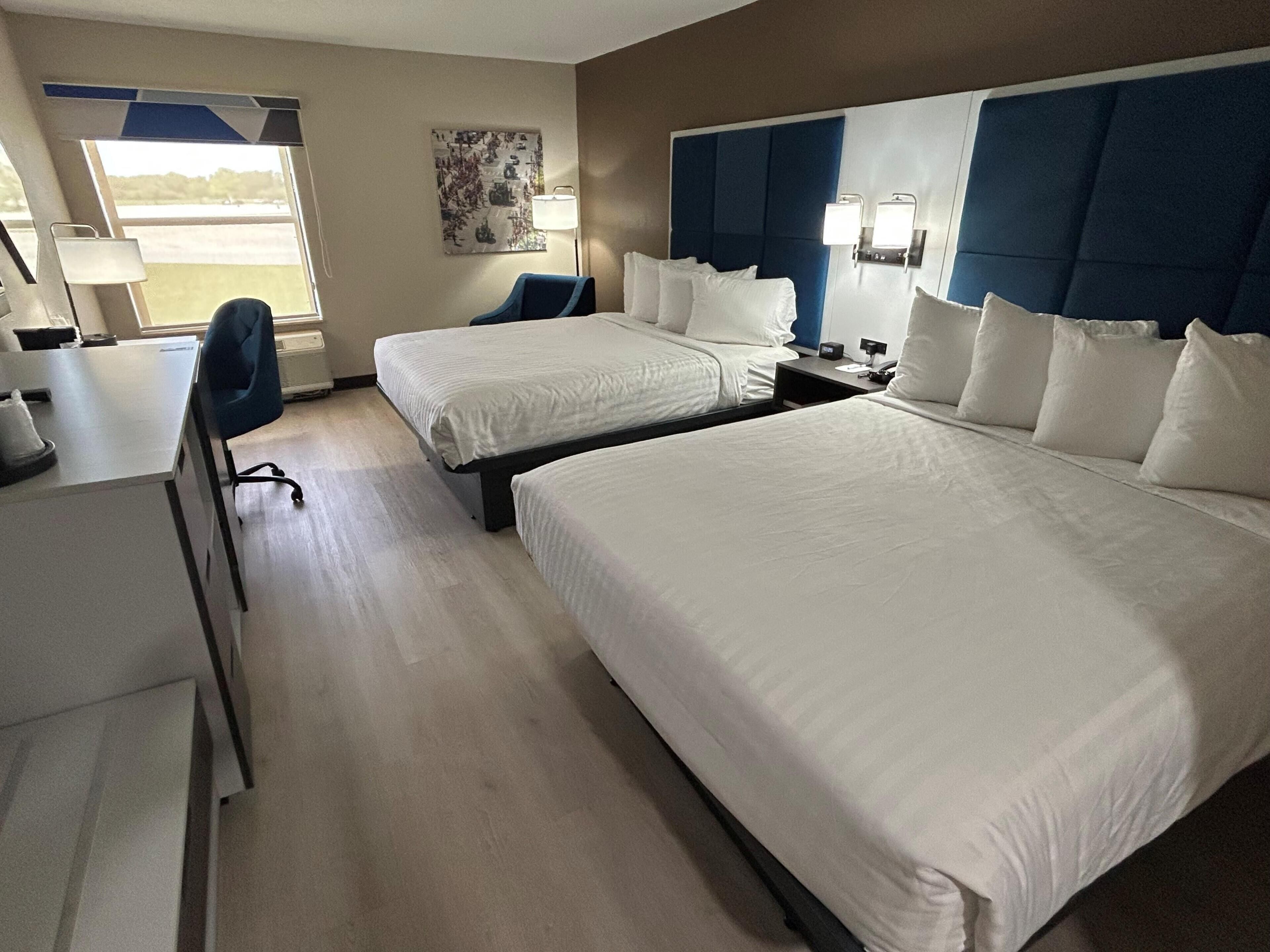 A hotel room with two beds, a desk, a chair, and a window with a view.