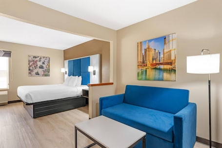 A hotel room with a bed, a blue sofa, a small table, and a painting of a cityscape.