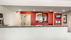 Ein Empfangsbereich mit einer Marmor-Theke, einer roten Wand mit einem Baumgemälde, einer Tür und einem an der Wand montierten Fernseher.