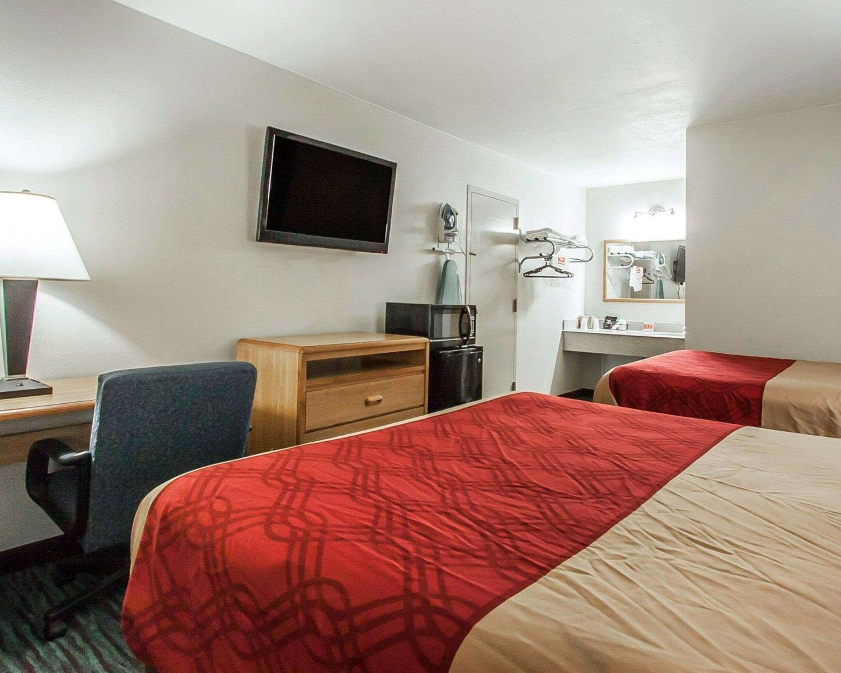 Una habitación de hotel con dos camas, un escritorio, una silla, un televisor, un espejo y una cómoda pequeña.