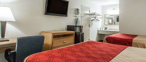 Una habitación de hotel con dos camas, un escritorio, una silla, un televisor, un espejo y una cómoda pequeña.