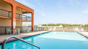 Ein Swimmingpool mit einer Metallleiter, umgeben von Stühlen und einem eingezäunten Bereich.