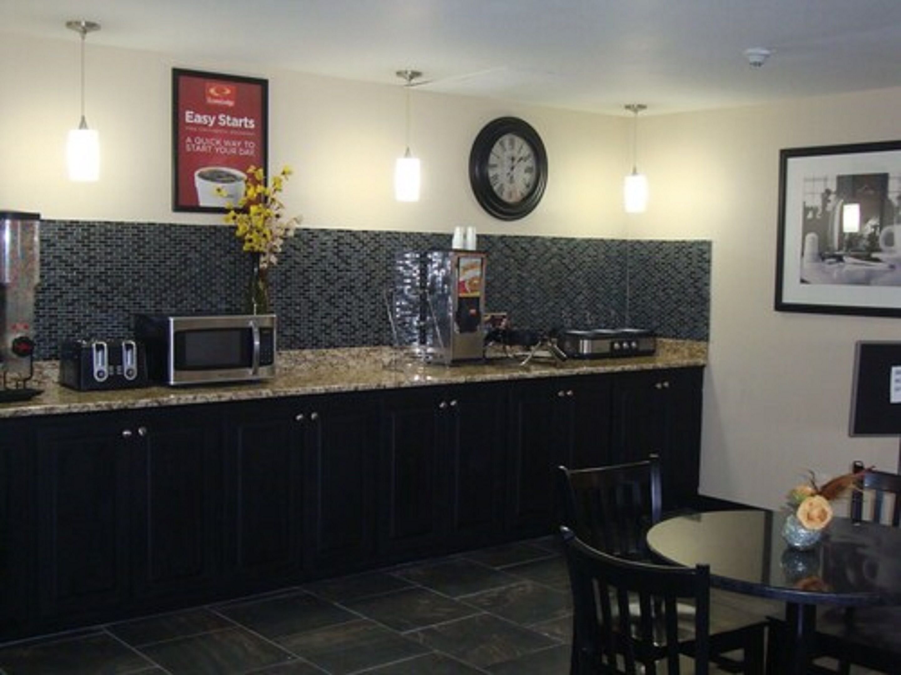 A modern kitchen with dark cabinets, a microwave, toaster, and a clock on the wall.