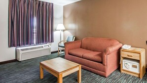 Ein Hotelzimmer mit einer Couch, einem Holztisch, einer Lampe, einem Heizgerät und einem Nachttisch mit Telefon und Radio.