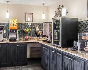 A kitchen with a refrigerator, a coffee machine, a fruit display, and a decorative rooster.