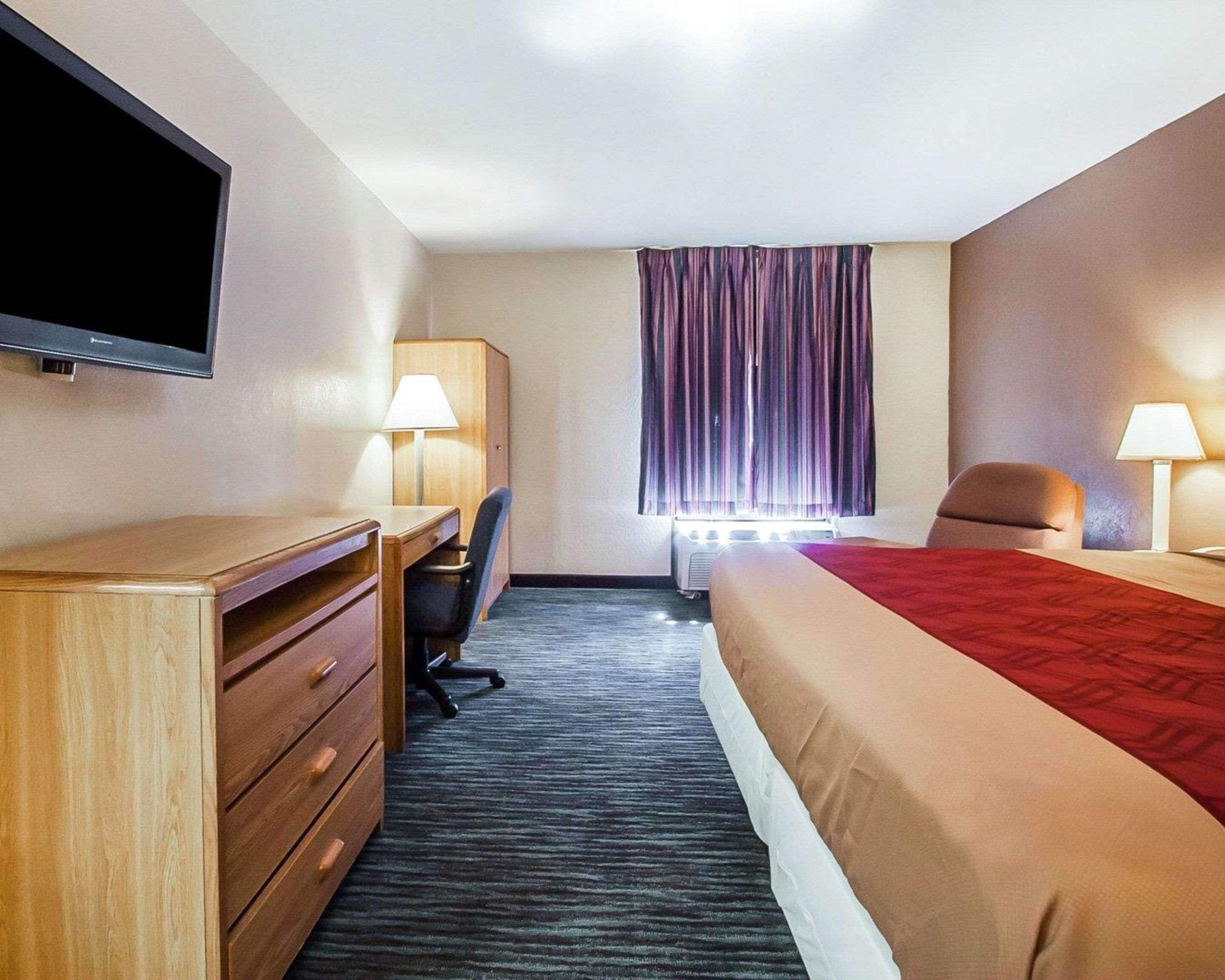 Una habitación de hotel con una cama, un escritorio con una silla, un televisor montado en la pared y dos lámparas de noche.