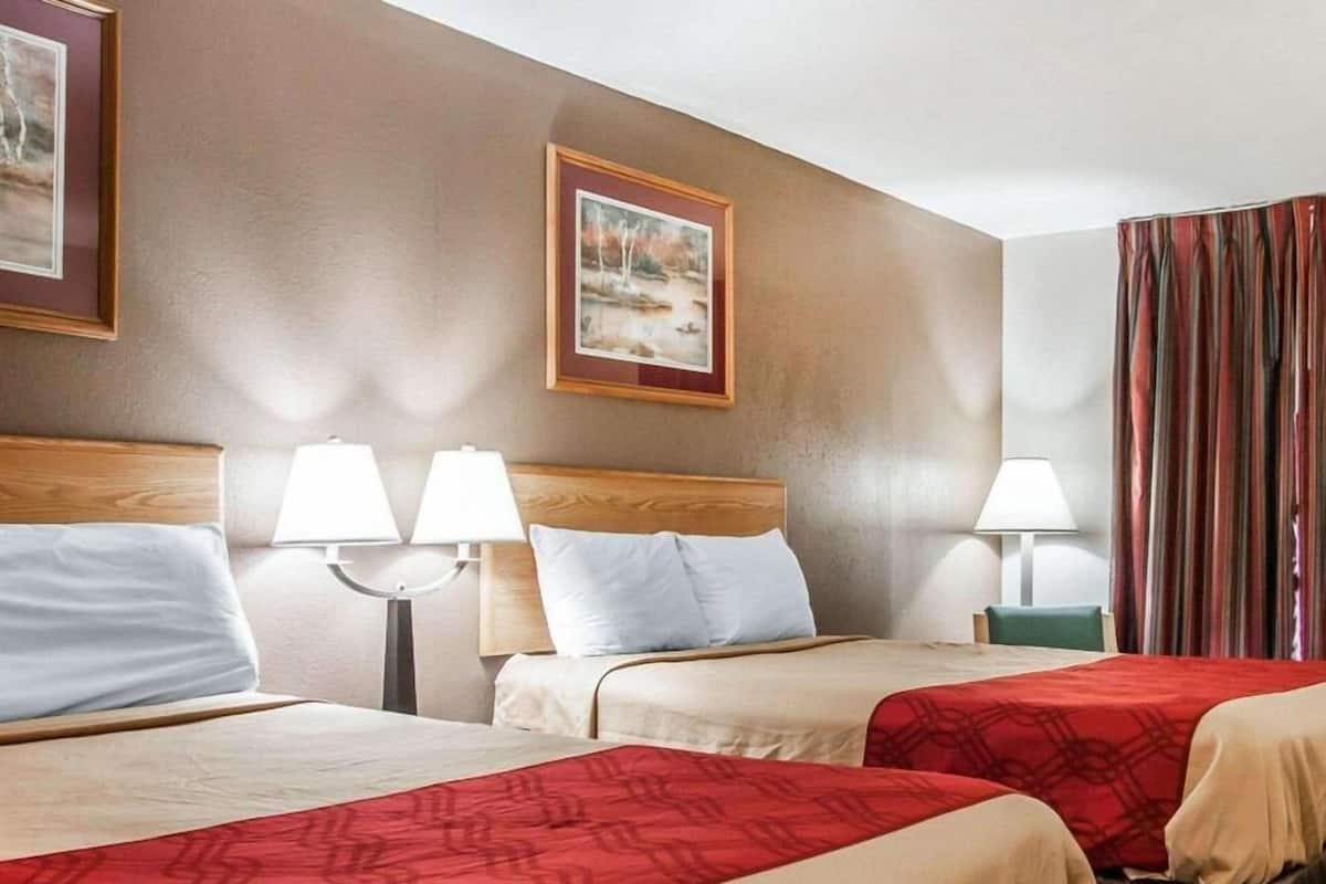 A hotel room with two beds, a headboard, bedside lamps, a framed picture on the wall, and a striped curtain.