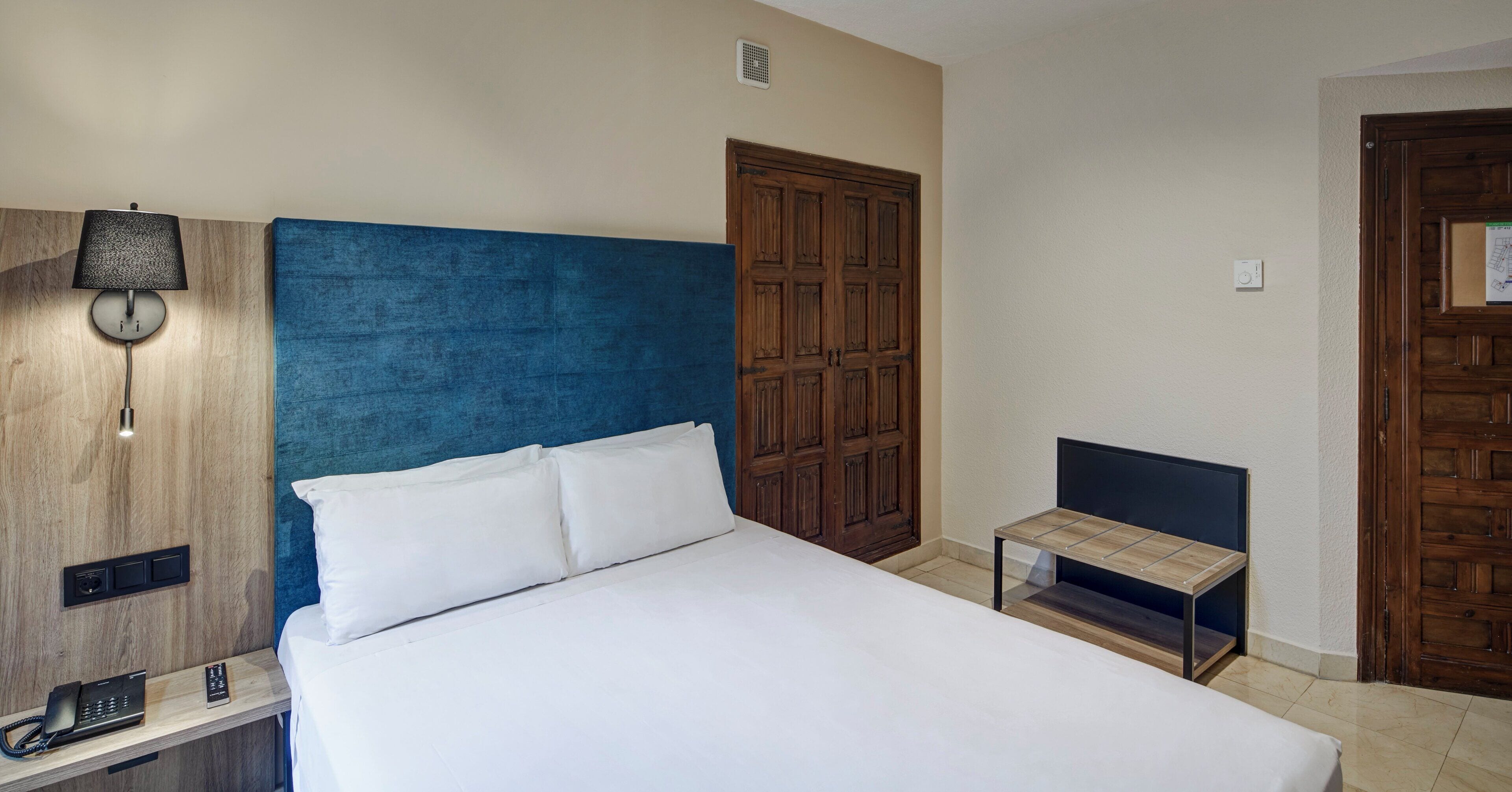 Una habitación de hotel con cama, mesita de noche, lámpara y armario.