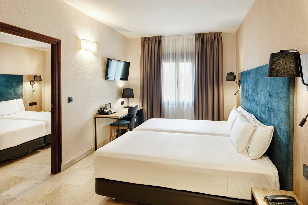 Une chambre d’hôtel avec deux lits, un bureau, une chaise, une télévision et un miroir.