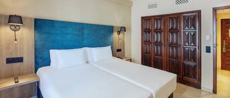 Una habitación de hotel con una cama grande, cabecero de madera, dos lámparas de noche, un armario de madera y una mesita de noche.