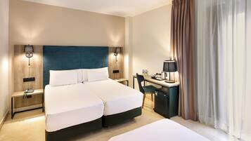A hotel room with a double bed, a desk with a chair, a small refrigerator, and two bedside tables with lamps.