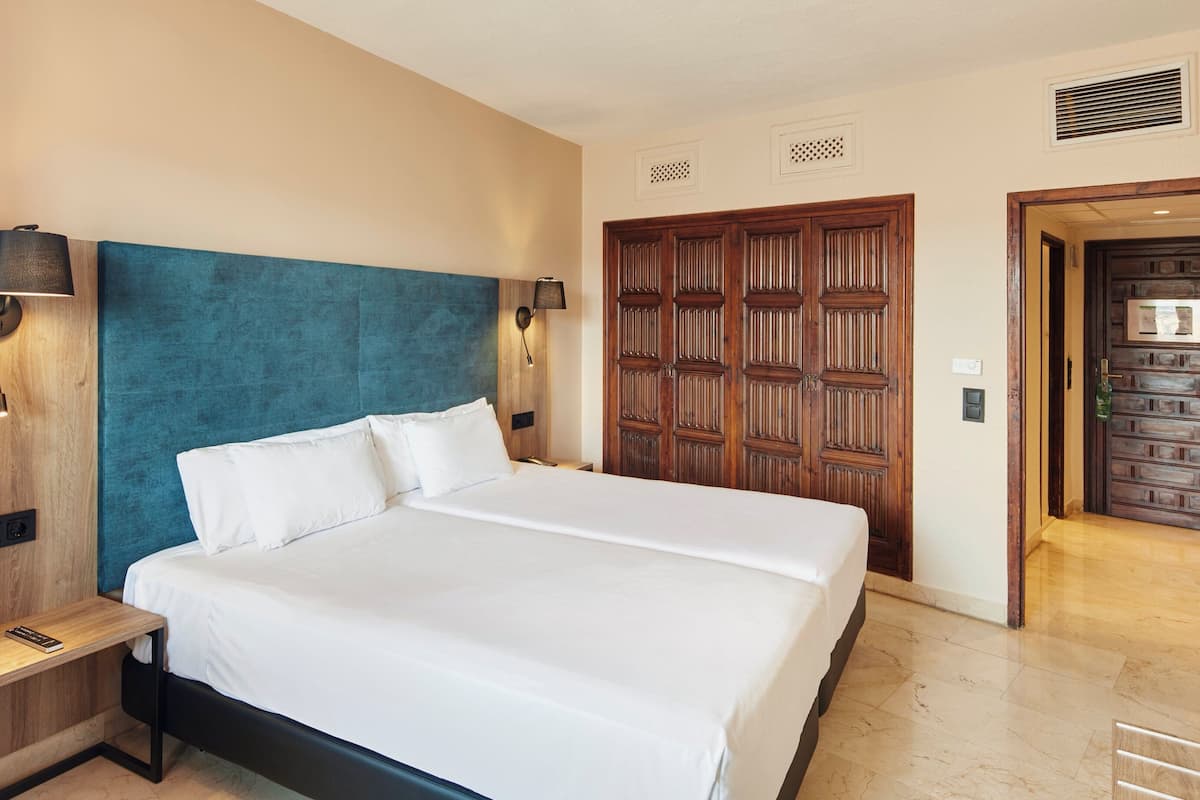 Ein Hotelzimmer mit einem großen Bett, einem Holzkopfstück, zwei Wandlampen, einem Nachttisch und einer Tür mit dekorativer Zarge.