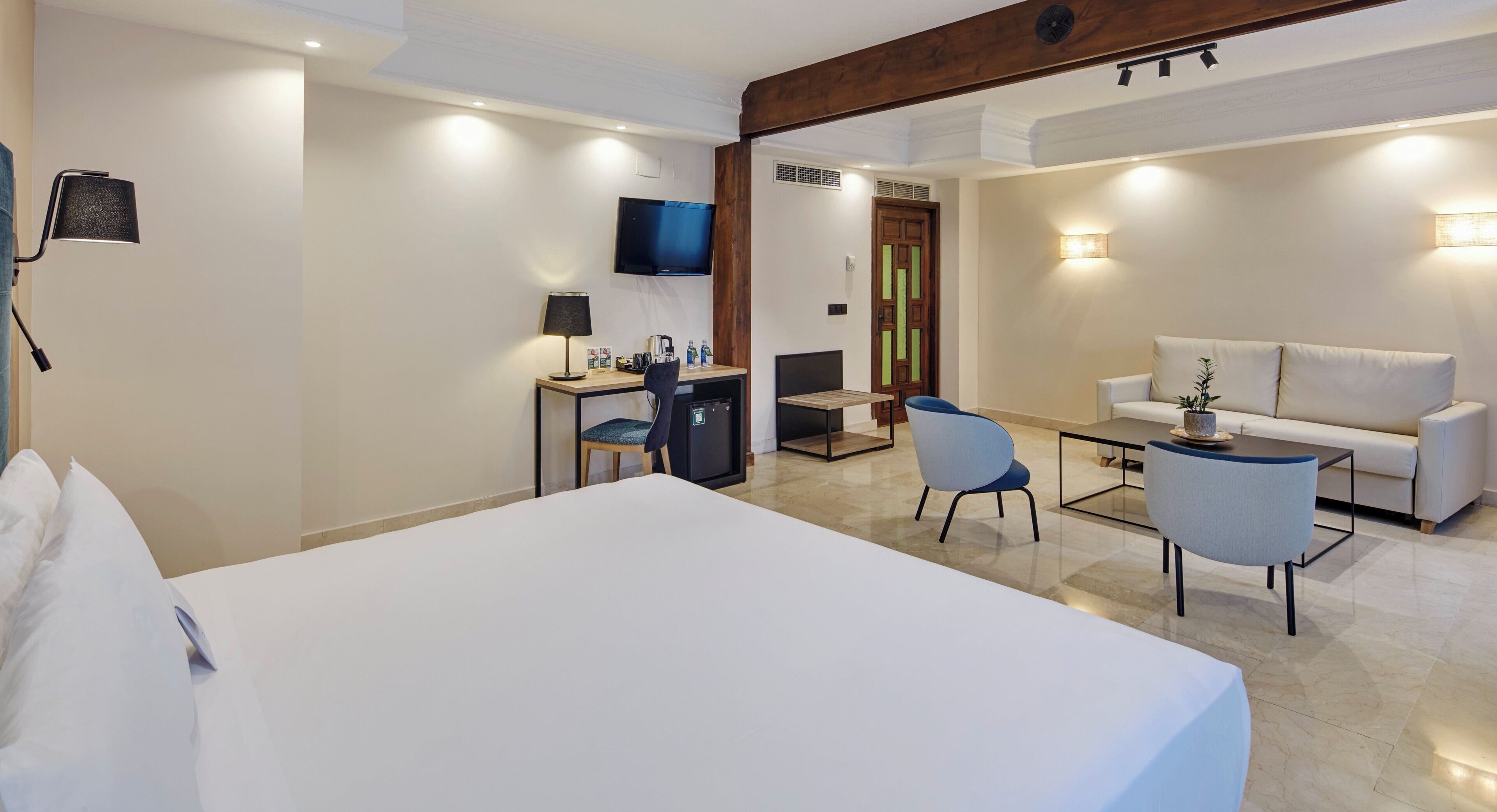 Una habitación de hotel con una cama grande, un escritorio con una silla, televisión, un sofá y una mesa de centro.