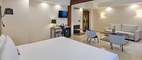 Una habitación de hotel con una cama grande, un escritorio con una silla, televisión, un sofá y una mesa de centro.