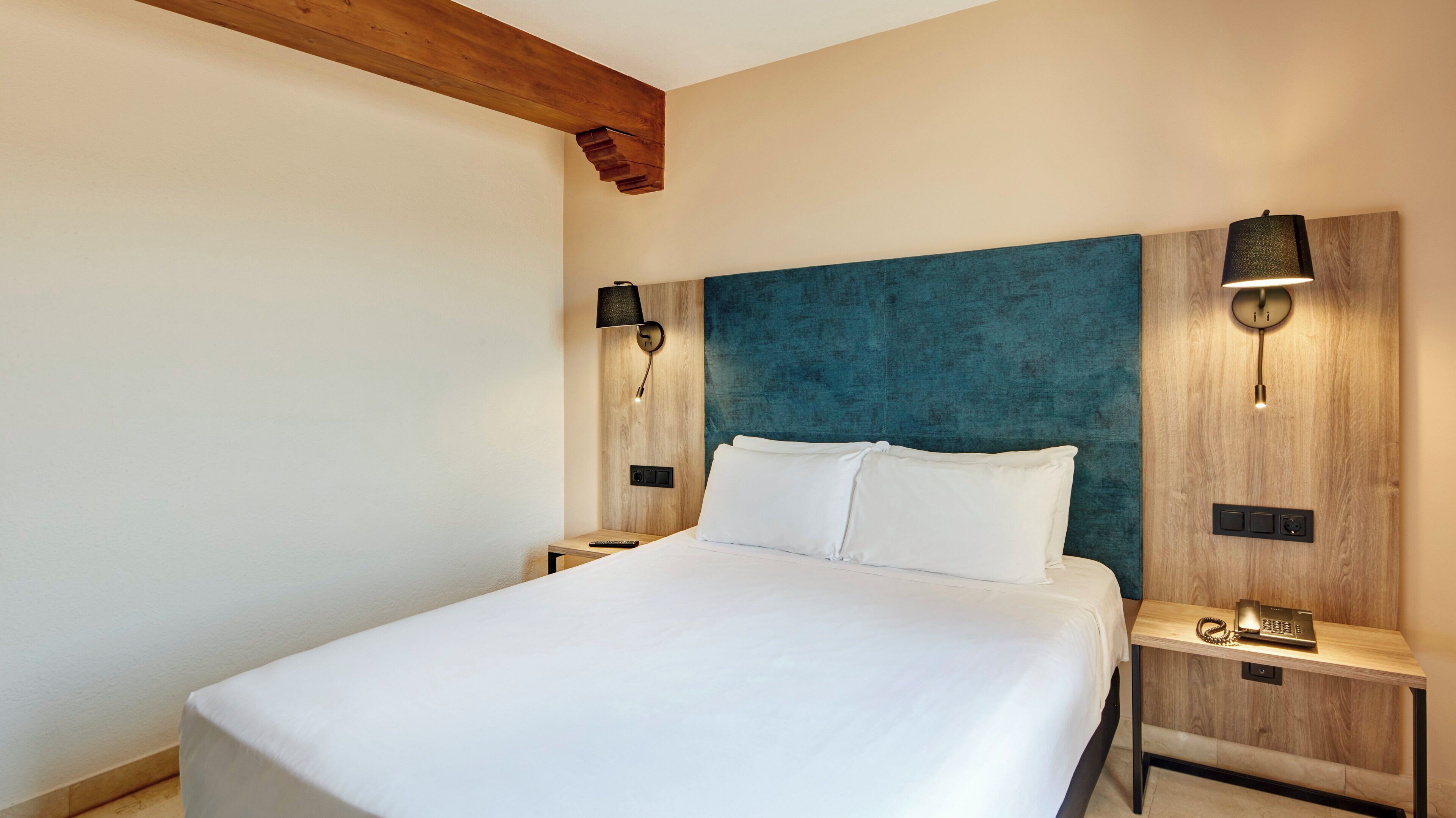 Een hotelkamer met een groot bed, twee nachtkastjes, een houten hoofdbord en wandlampen.